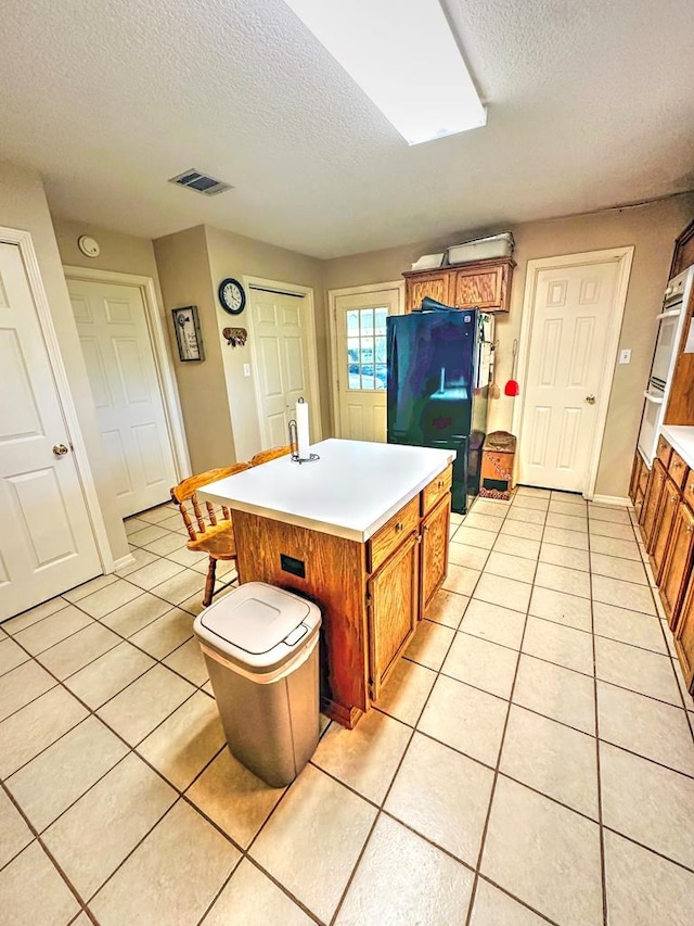 kitchen with a kitchen bar, a textured ceiling, a center island with sink, and light tile patterned flooring