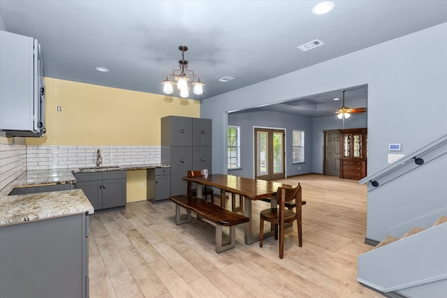 dining space with ceiling fan with notable chandelier, french doors, sink, and light hardwood / wood-style flooring