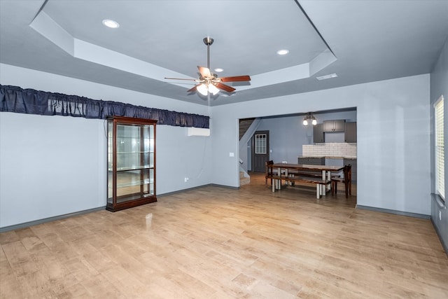 living room featuring ceiling fan, a raised ceiling, and light wood-type flooring