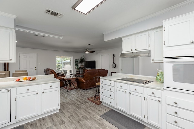 kitchen with white oven, black electric cooktop, white cabinets, under cabinet range hood, and visible vents