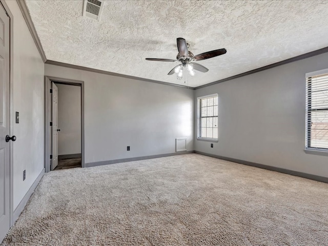 empty room featuring a textured ceiling, carpet floors, visible vents, and crown molding