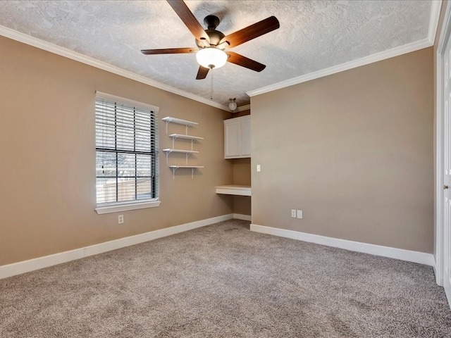 empty room with a textured ceiling, light colored carpet, baseboards, built in desk, and crown molding