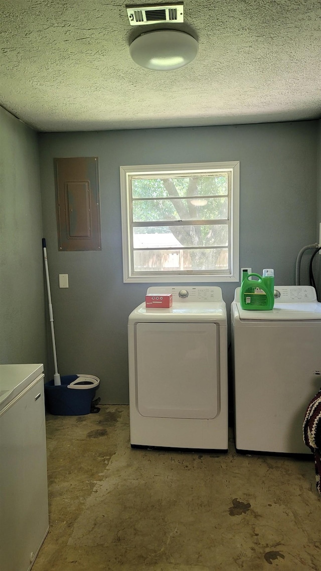 washroom featuring washing machine and clothes dryer, electric panel, and a textured ceiling