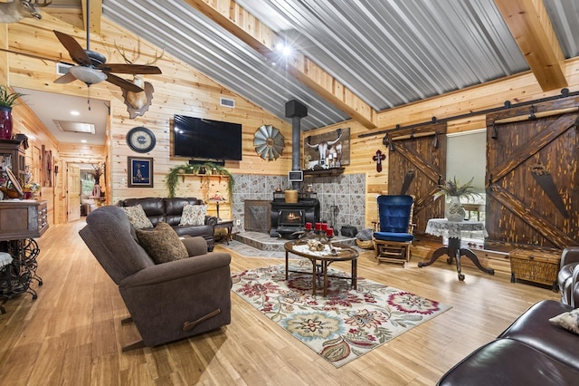 living room featuring a wood stove, wooden walls, ceiling fan, light wood-type flooring, and beam ceiling