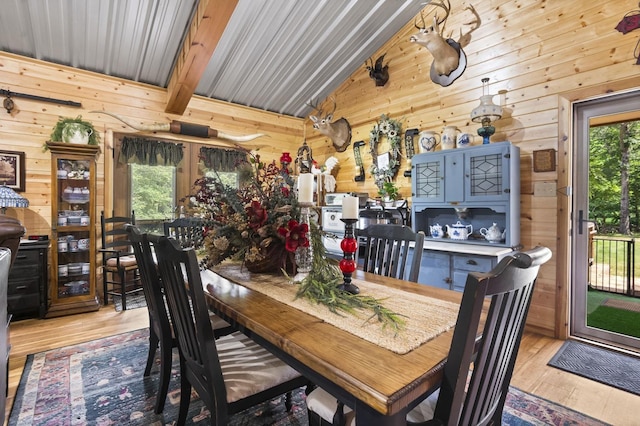 dining room with lofted ceiling with beams, wooden walls, and light hardwood / wood-style flooring