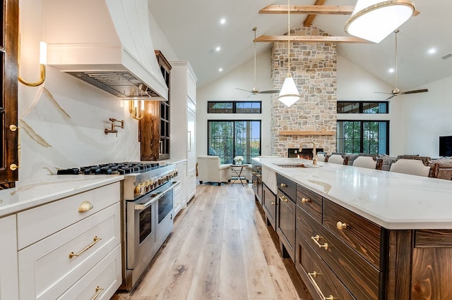 kitchen with double oven range, custom exhaust hood, a sink, white cabinetry, and open floor plan