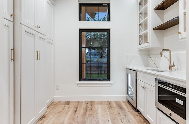 kitchen with a sink, open shelves, wine cooler, white cabinets, and light wood finished floors