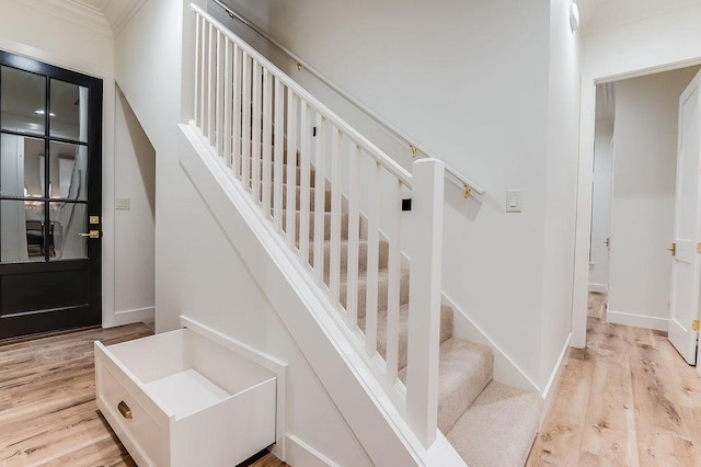 staircase featuring wood finished floors, baseboards, and ornamental molding