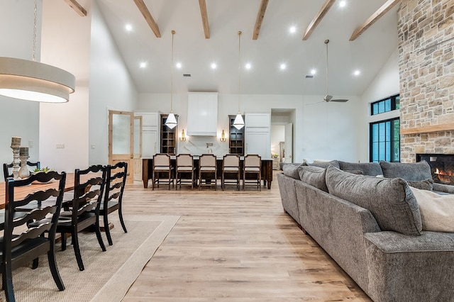 living area featuring beamed ceiling, a fireplace, high vaulted ceiling, and light wood-type flooring