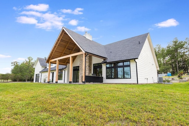 rear view of property with a lawn, central AC unit, a chimney, and a shingled roof