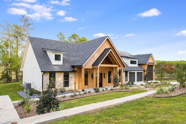 modern inspired farmhouse with a shingled roof, a front lawn, central air condition unit, a porch, and stone siding