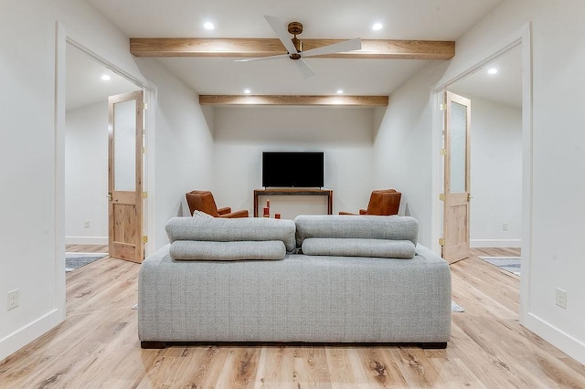 living room featuring beamed ceiling, baseboards, light wood-style flooring, and a ceiling fan