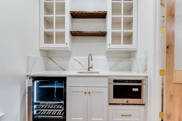 kitchen with beverage cooler, a sink, glass insert cabinets, white cabinetry, and stainless steel oven