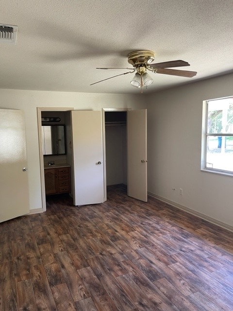 unfurnished bedroom featuring connected bathroom, ceiling fan, dark wood-type flooring, and a textured ceiling