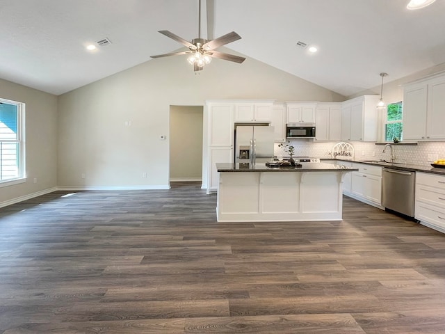kitchen featuring a ceiling fan, dark countertops, a sink, stainless steel appliances, and a kitchen island