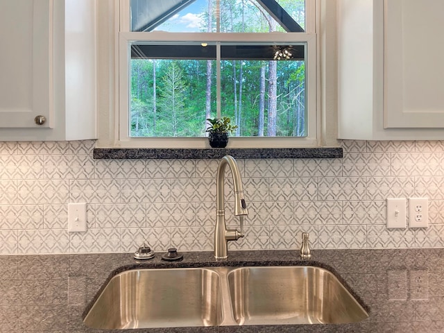 details with white cabinets, decorative backsplash, a sink, and dark stone counters