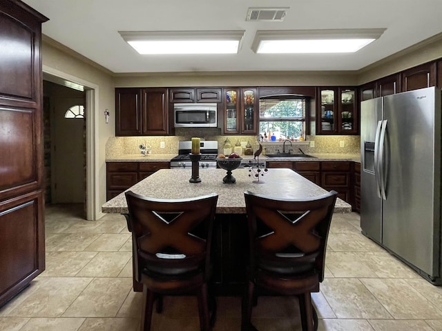 kitchen featuring a kitchen breakfast bar, sink, appliances with stainless steel finishes, dark brown cabinets, and a kitchen island