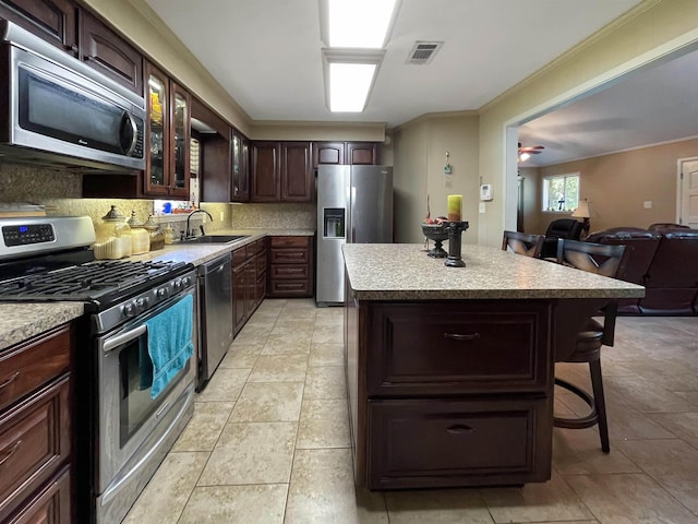 kitchen featuring ceiling fan, sink, appliances with stainless steel finishes, a kitchen island, and ornamental molding