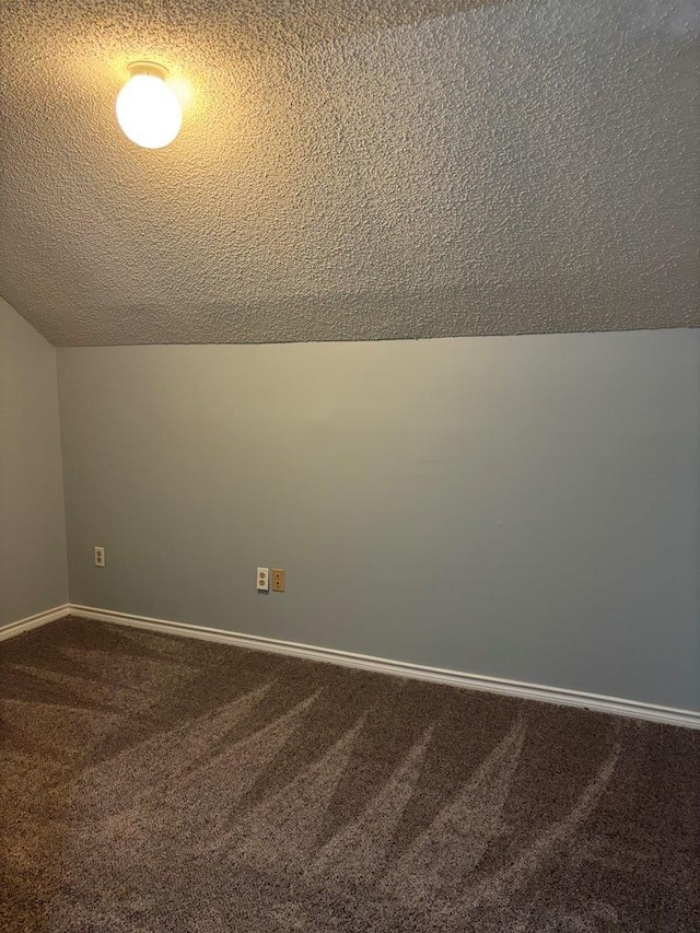 unfurnished room featuring baseboards, dark carpet, vaulted ceiling, and a textured ceiling