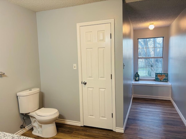 bathroom with a textured ceiling, wood finished floors, toilet, and baseboards