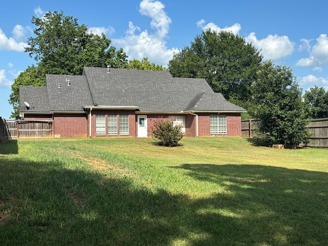 back of house with roof with shingles, brick siding, a lawn, and fence