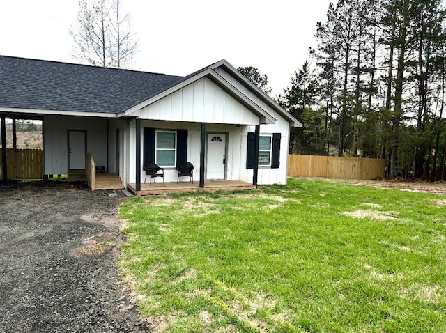 view of front facade with roof with shingles, board and batten siding, a front yard, and fence