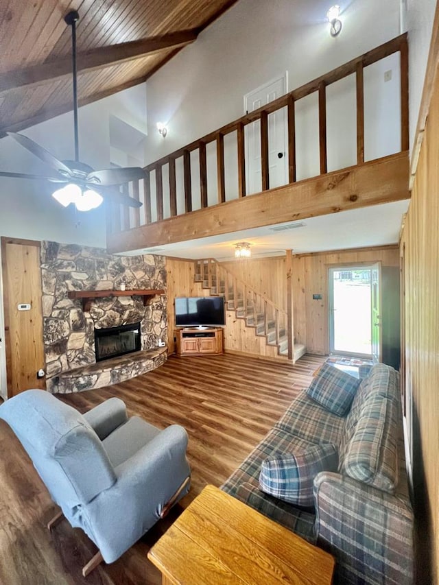 living room featuring ceiling fan, high vaulted ceiling, a fireplace, hardwood / wood-style floors, and wood walls