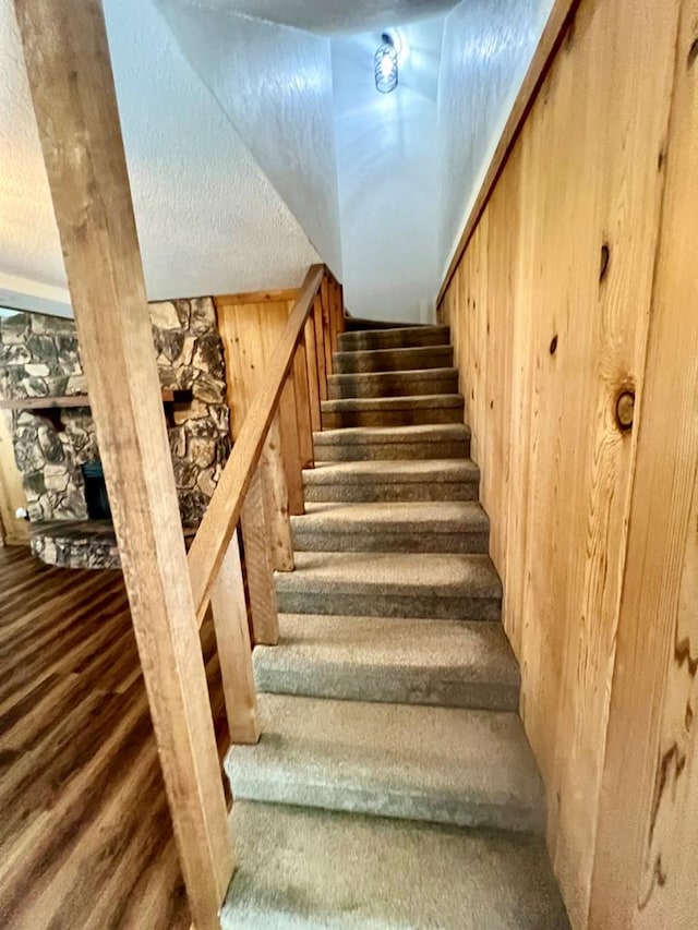 stairs with wood-type flooring, a textured ceiling, and wood walls