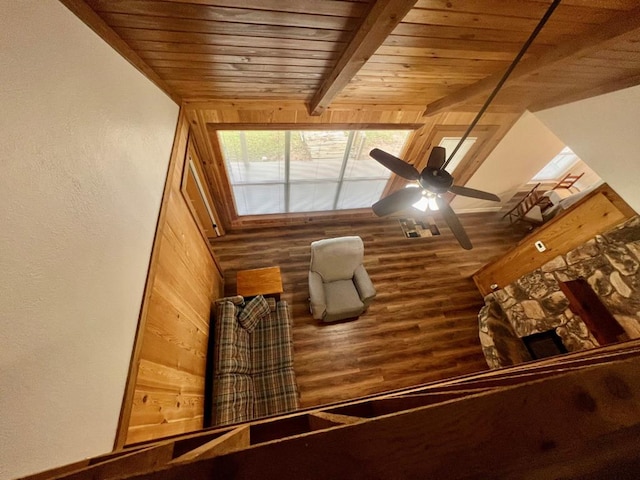 interior space featuring wood ceiling, ceiling fan, beamed ceiling, a stone fireplace, and wood walls