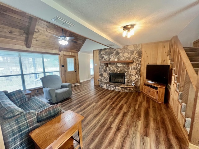 living room featuring lofted ceiling with beams, a stone fireplace, ceiling fan, a textured ceiling, and dark hardwood / wood-style flooring