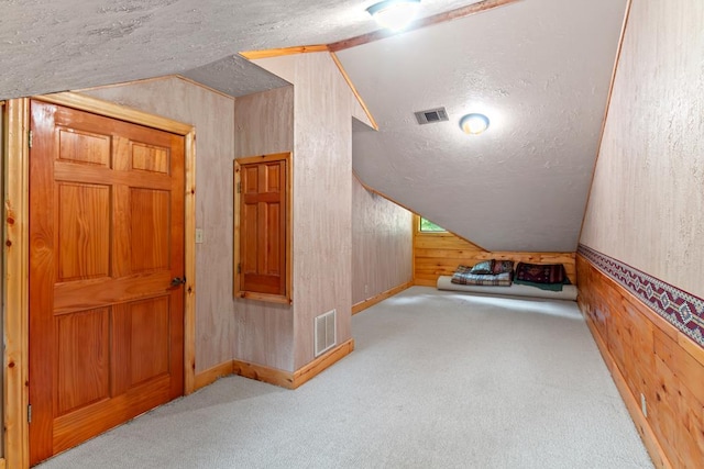 bonus room with wood walls, lofted ceiling, a textured ceiling, and light carpet