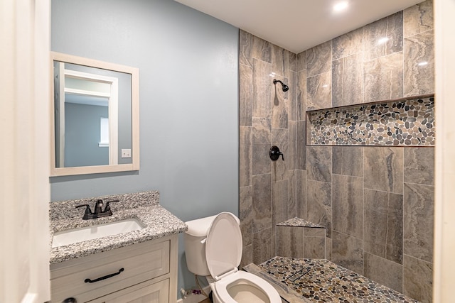 full bath featuring toilet, a tile shower, and vanity
