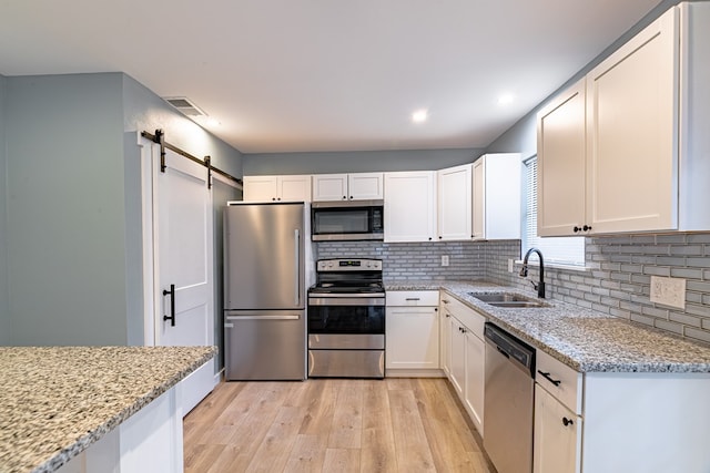 kitchen with appliances with stainless steel finishes, a sink, light wood finished floors, a barn door, and decorative backsplash