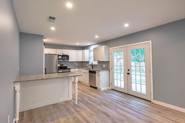 kitchen featuring appliances with stainless steel finishes, a sink, french doors, white cabinets, and tasteful backsplash