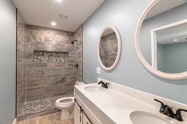full bath featuring toilet, tiled shower, double vanity, wood finished floors, and recessed lighting