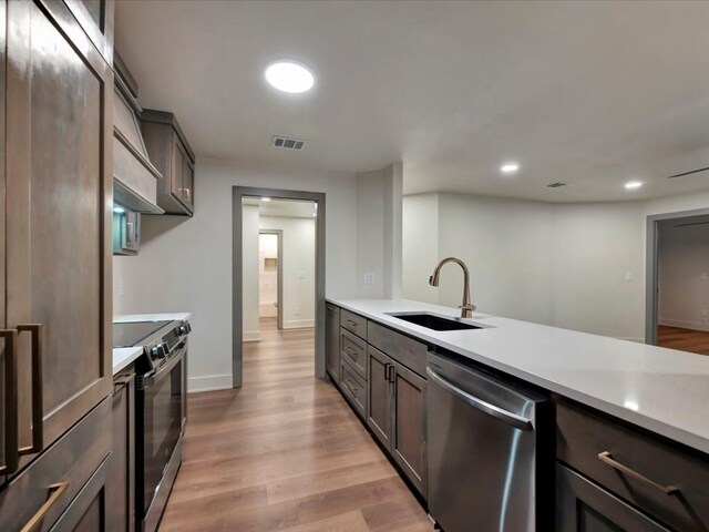 kitchen featuring dark brown cabinetry, sink, stainless steel appliances, tasteful backsplash, and premium range hood