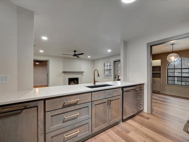 kitchen featuring pendant lighting, sink, stainless steel dishwasher, light hardwood / wood-style floors, and kitchen peninsula