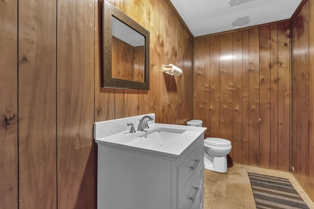 bathroom featuring tile patterned flooring, wooden walls, vanity, a textured ceiling, and toilet