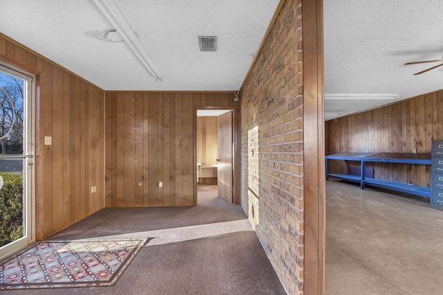 hall featuring wooden walls and a textured ceiling