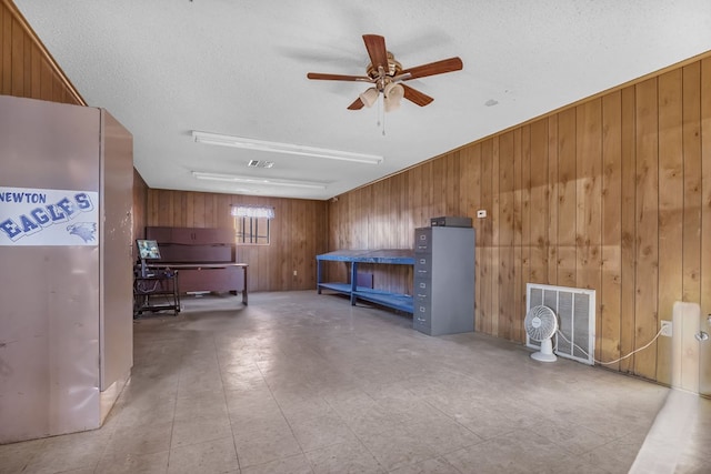 misc room featuring ceiling fan, a textured ceiling, and wooden walls