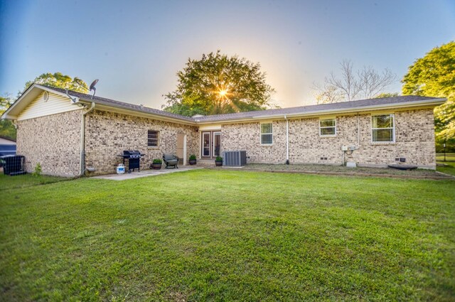 back of house at dusk with a patio, a yard, brick siding, and central AC