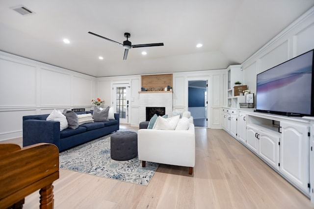 living room with ceiling fan, a brick fireplace, lofted ceiling, and light wood-type flooring