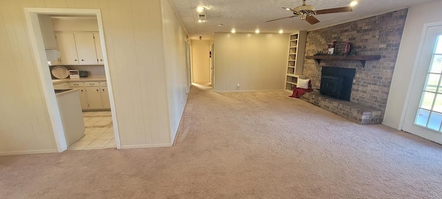 unfurnished living room with ceiling fan, light colored carpet, a textured ceiling, and a brick fireplace