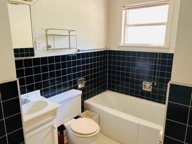 bathroom featuring vanity, a bath, tile patterned floors, toilet, and tile walls