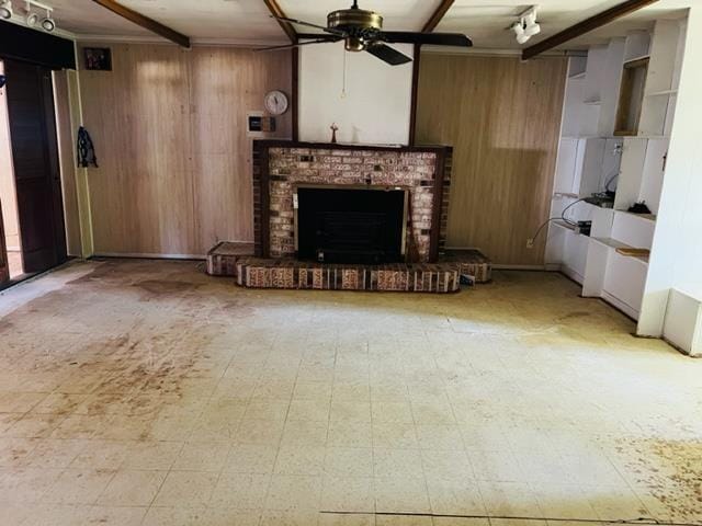 unfurnished living room with ceiling fan, beam ceiling, a fireplace, and wooden walls