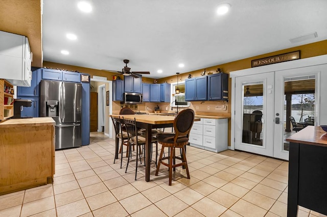 kitchen with a breakfast bar, blue cabinetry, light tile patterned floors, stainless steel appliances, and wooden counters