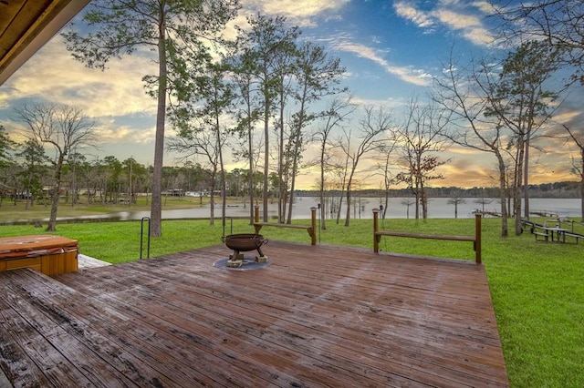 deck at dusk featuring a yard, a water view, and a covered hot tub