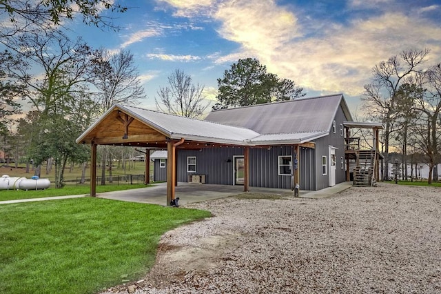 exterior space featuring gravel driveway, a yard, board and batten siding, metal roof, and stairs