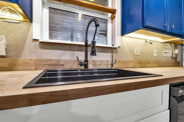 kitchen featuring blue cabinetry, black dishwasher, and a sink