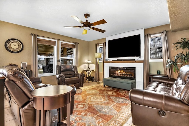 living room with a textured ceiling, a glass covered fireplace, and a ceiling fan